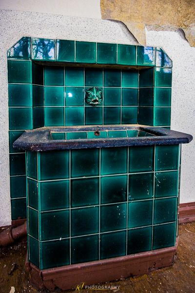 Eine grüne geflieste Küche mit einem Waschbecken und einem kaputten Fae