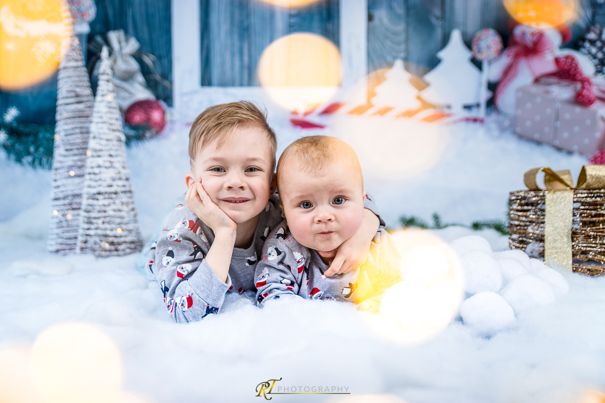 Zwei Kinder sitzen im Schnee mit Weihnachtsbeleuchtung