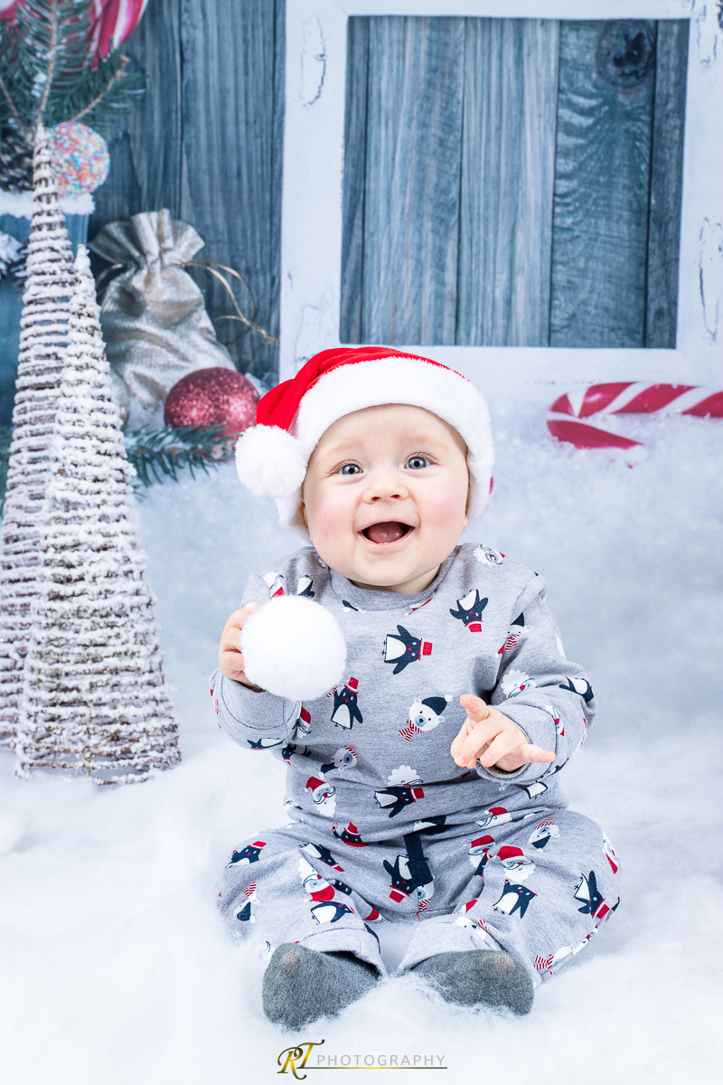 Ein Baby in einem Weihnachtshut im Schnee sitzend